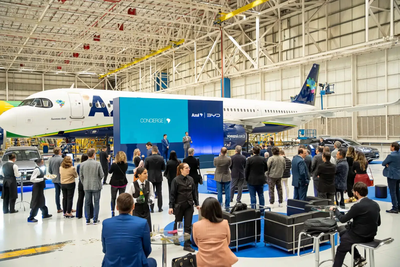 Lançamento do Concierge BYD e Azul em hangar, com convidados e aeronave ao fundo